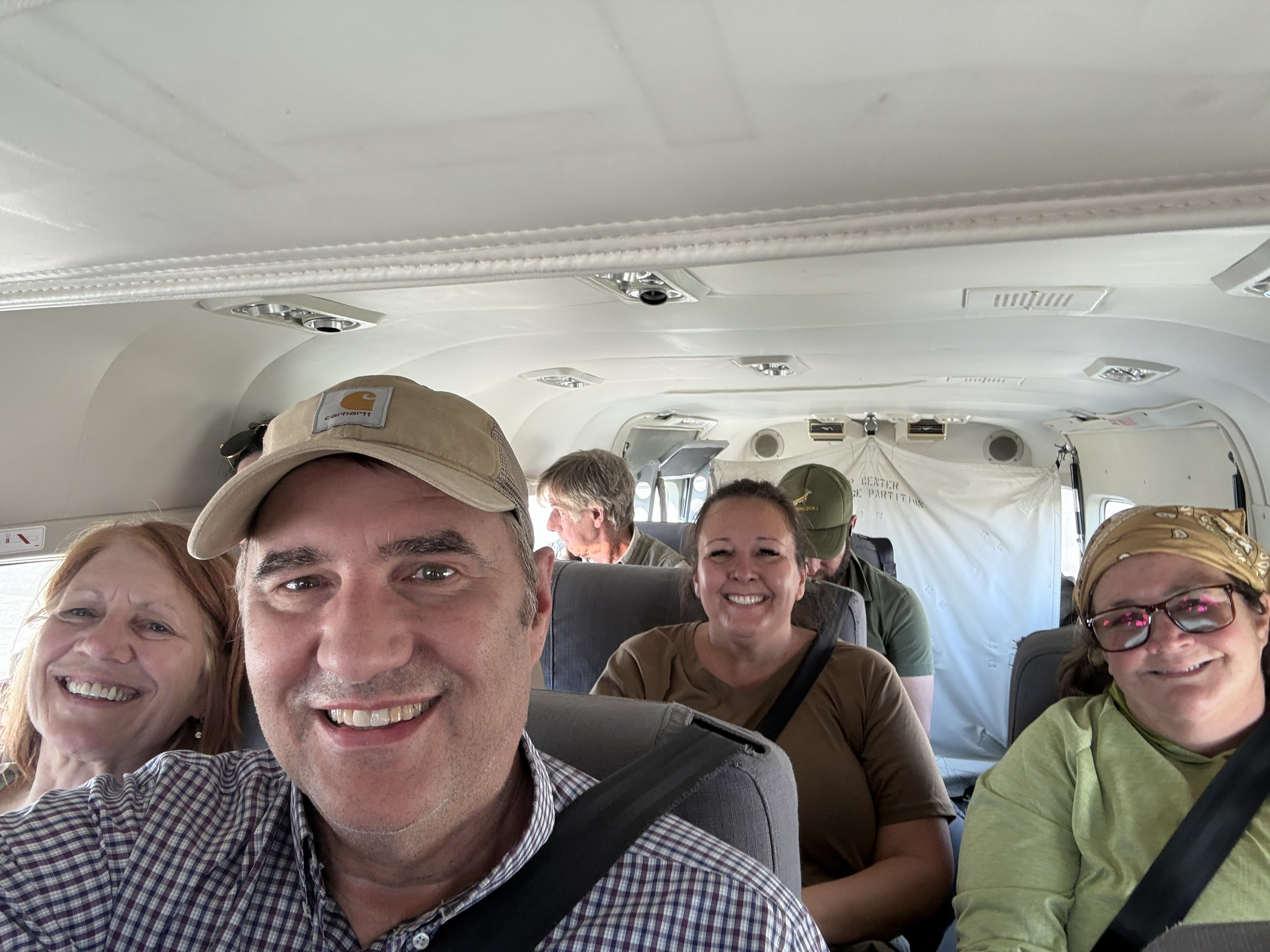 The cabin — knees together, cameras up, everybody grinning like children, which is the only correct response to a bush flight.