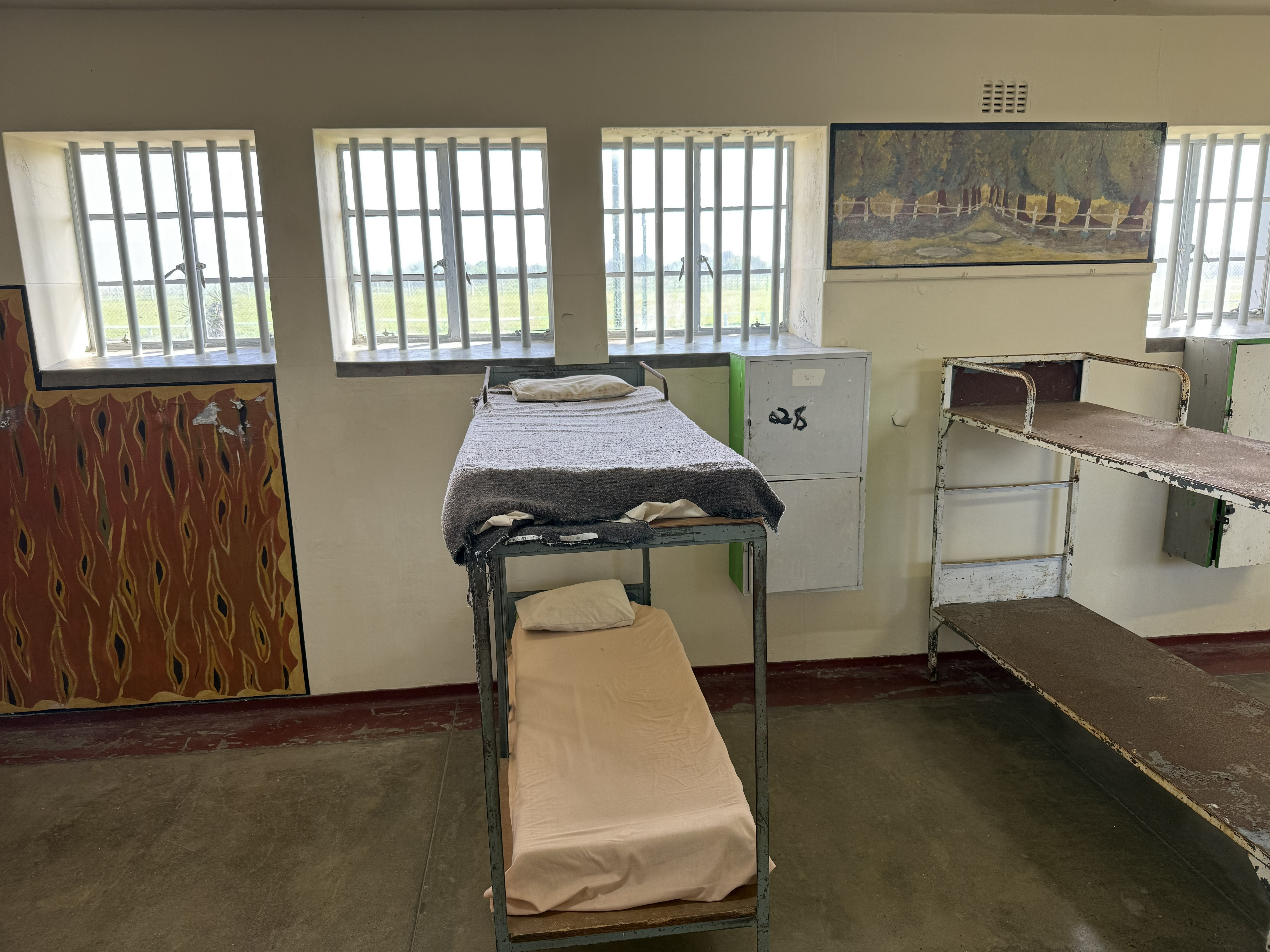 A cell in the communal block — a bed, a bucket, a window, and the years.